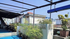En tagterrasse med et blåt poolområde, plantekasser og udsigt til omkringliggende bygninger.