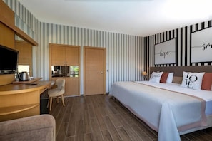 A hotel room with a bed, desk, chair, and a kitchenette.