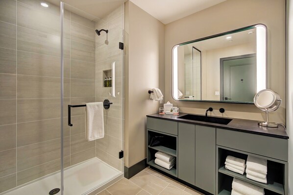 Un bany modern amb dutxa de vidre, un lavabo amb mirall i un paraigua de tovalloles.