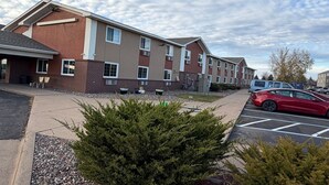 A multi-story building with a brick facade, large windows, and a parking lot with a red car. - Coratel Inn and Suites by Jasper Stillwater Standard 1 King Bed Non Smoking (Stillwater)