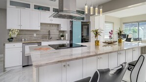Una cocina moderna con armarios blancos, encimera de mármol e iluminación colgante.