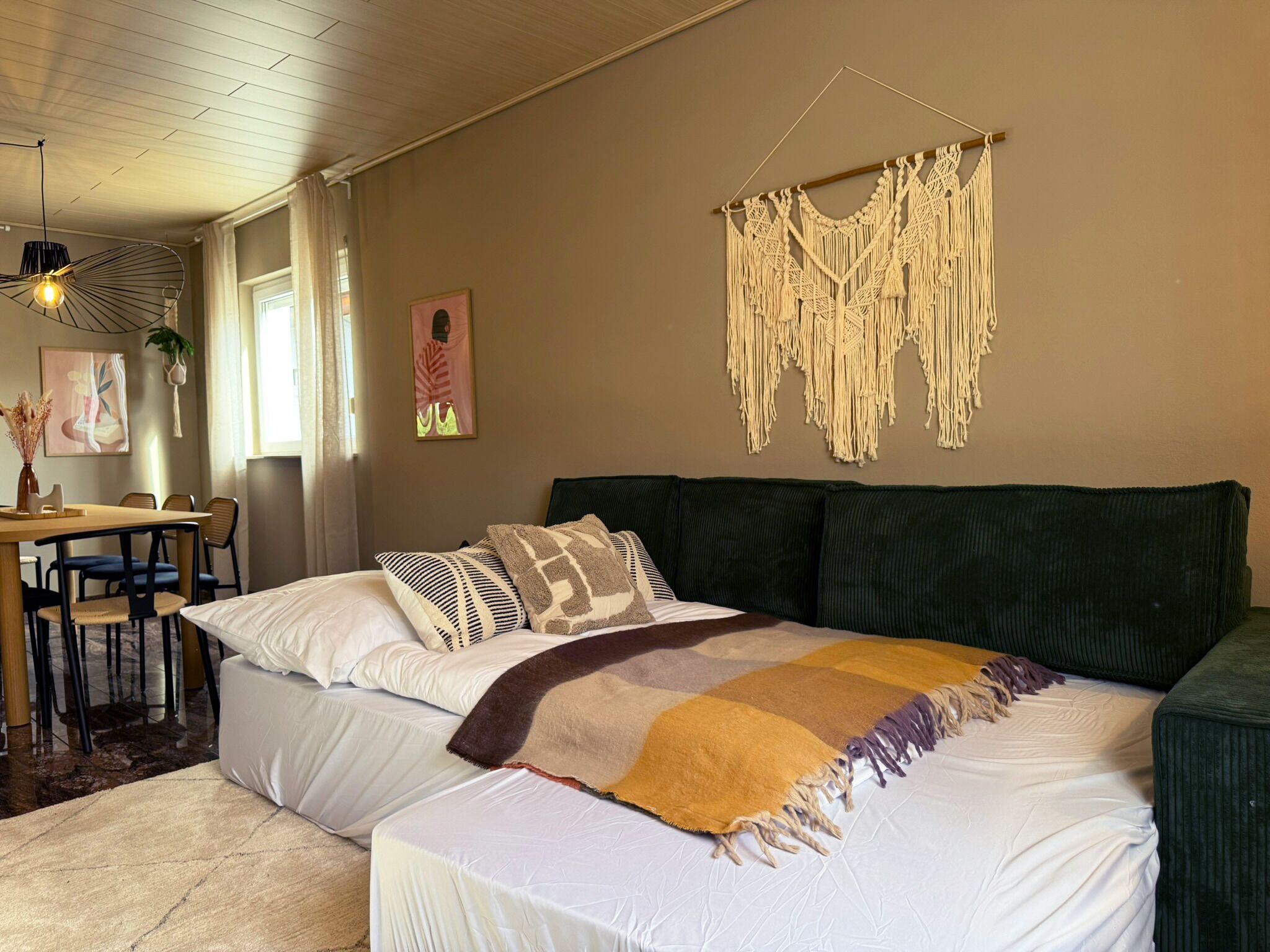 A bedroom with a bed, a desk, and a macrame wall hanging.