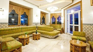 A spacious living room with a green sofa set, wooden side tables, and a large window with a view. - El Mouradi Mahdia (Mahdia)