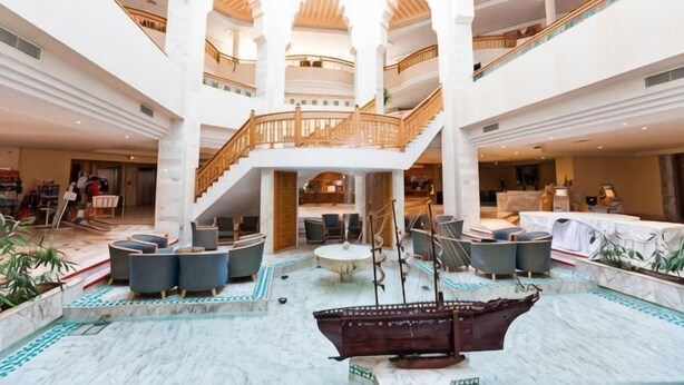 A multi-level atrium with a central staircase, seating areas, and a decorative ship model. - El Mouradi Mahdia (Mahdia)
