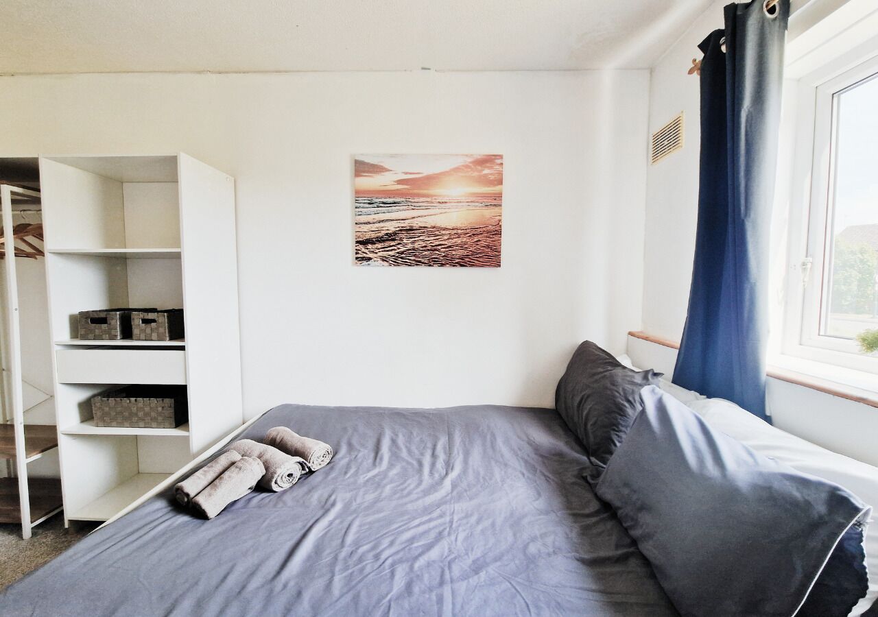 A bedroom with a bed, a white wardrobe, a window with curtains, and a picture on the wall.