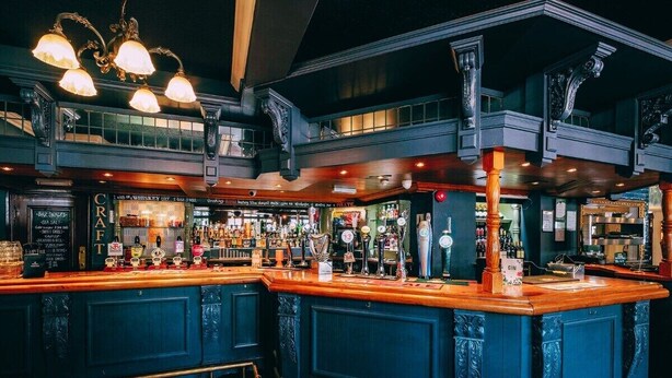 A bar with a wooden counter and blue cabinetry, featuring multiple liquor bottles and a variety of bar tools.