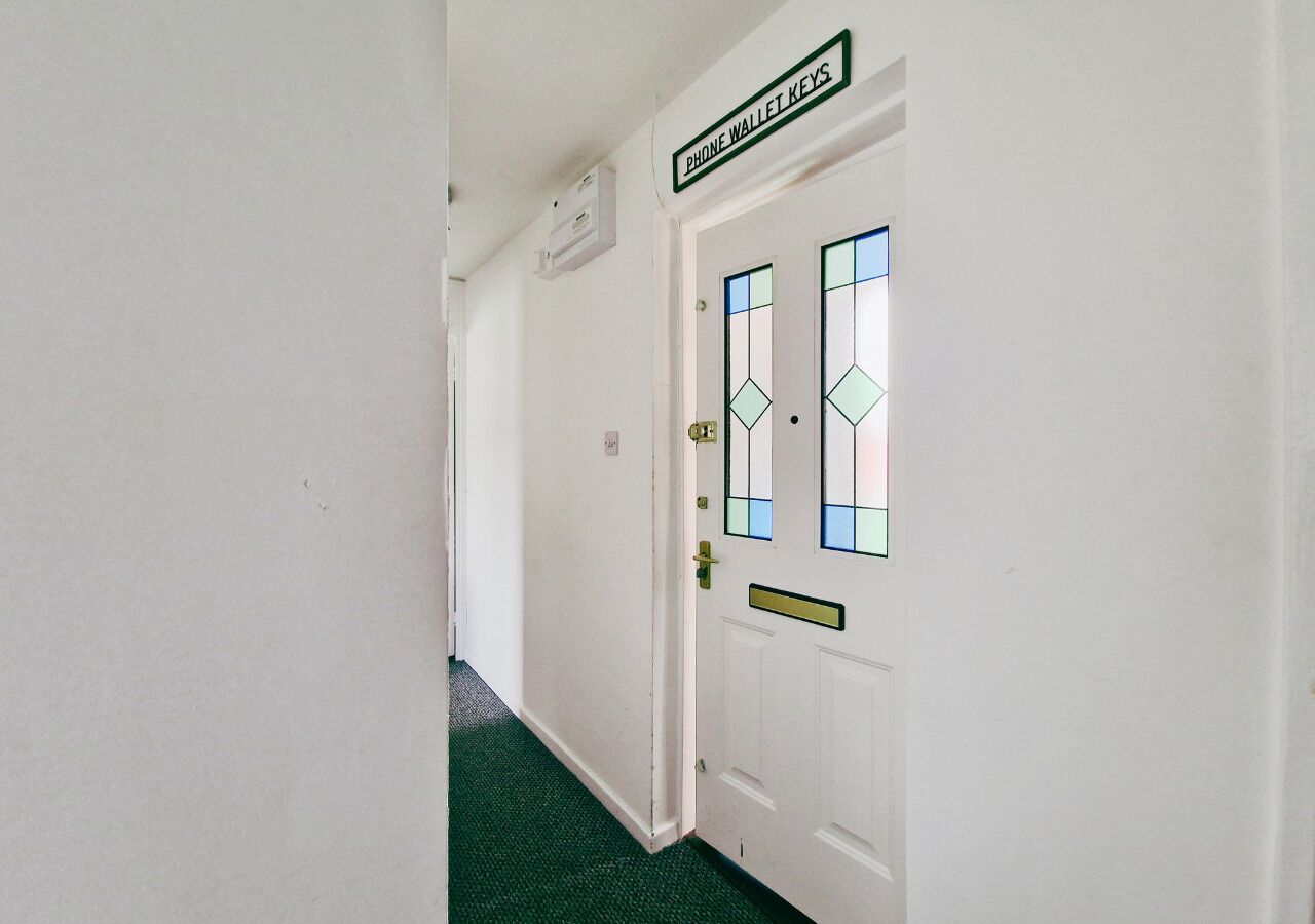 A hallway with a white door labeled 'Phone Wallet Keys,' a green carpet, and a white wall.