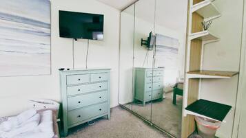A bedroom with a bed, a dresser, a television, a mirror, and a shelf unit.