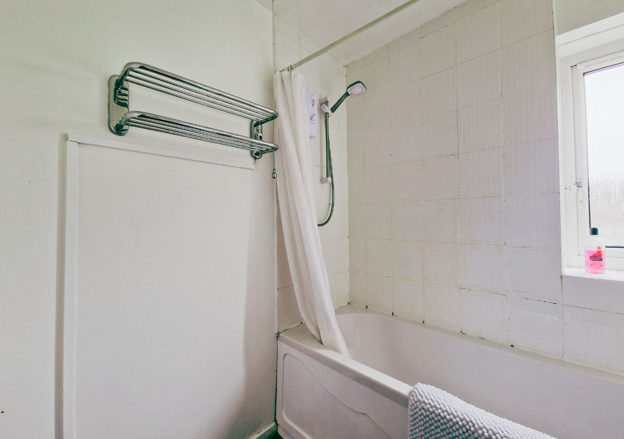 A bathroom with a shower, a towel rack, and a window.