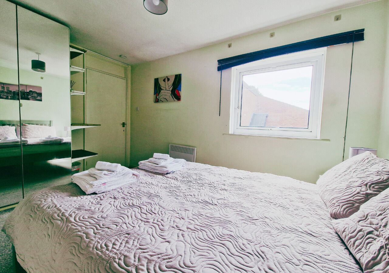 A bedroom with a large bed, a wardrobe, a window, and a painting on the wall.