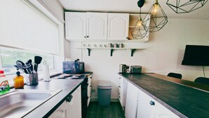 A compact kitchen with white cabinets, a sink, a stove, and a trash bin.