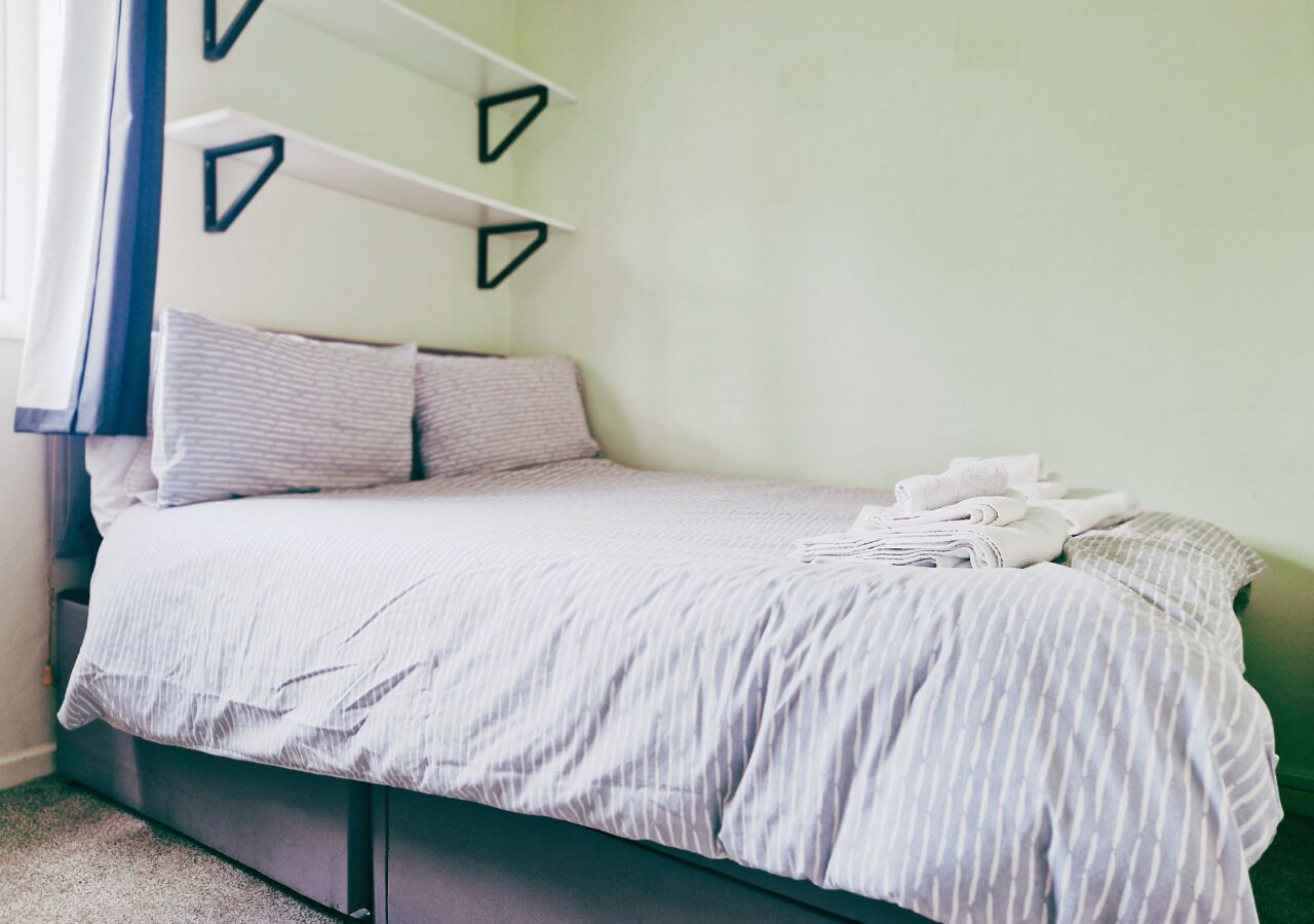 Un lit avec une couvre-lit à rayures, des oreillers et une serviette pliée, le tout posé sur un cadre de lit de couleur foncée.