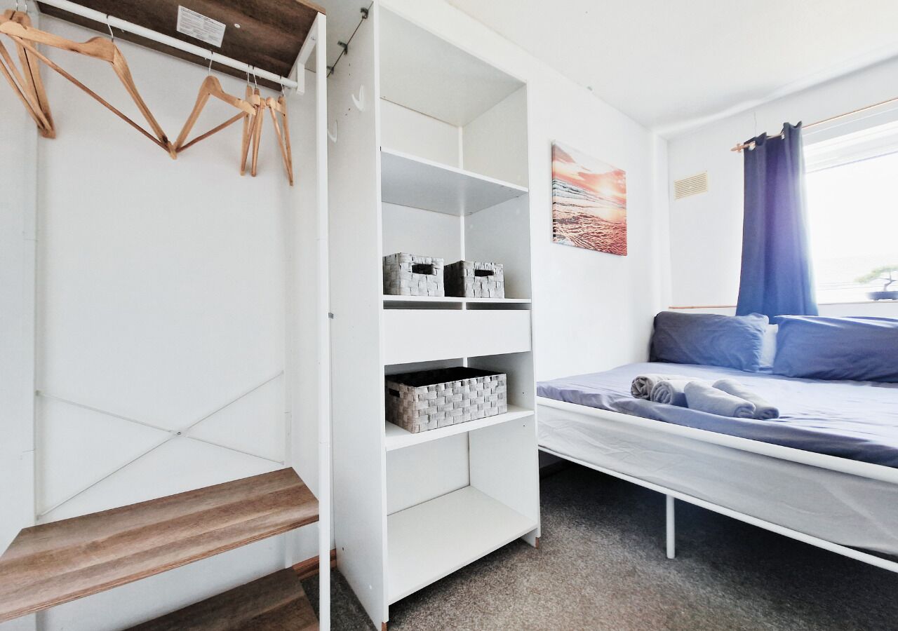 Une pièce avec un lit, une armoire blanche et une fenêtre avec des rideaux.