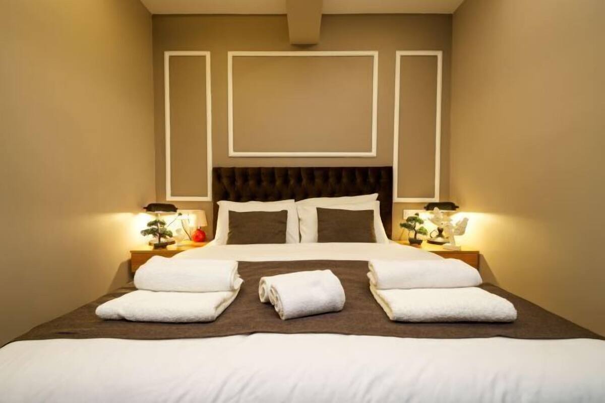 A neatly made bed with white linens and towels, a dark headboard, and bedside lamps.
