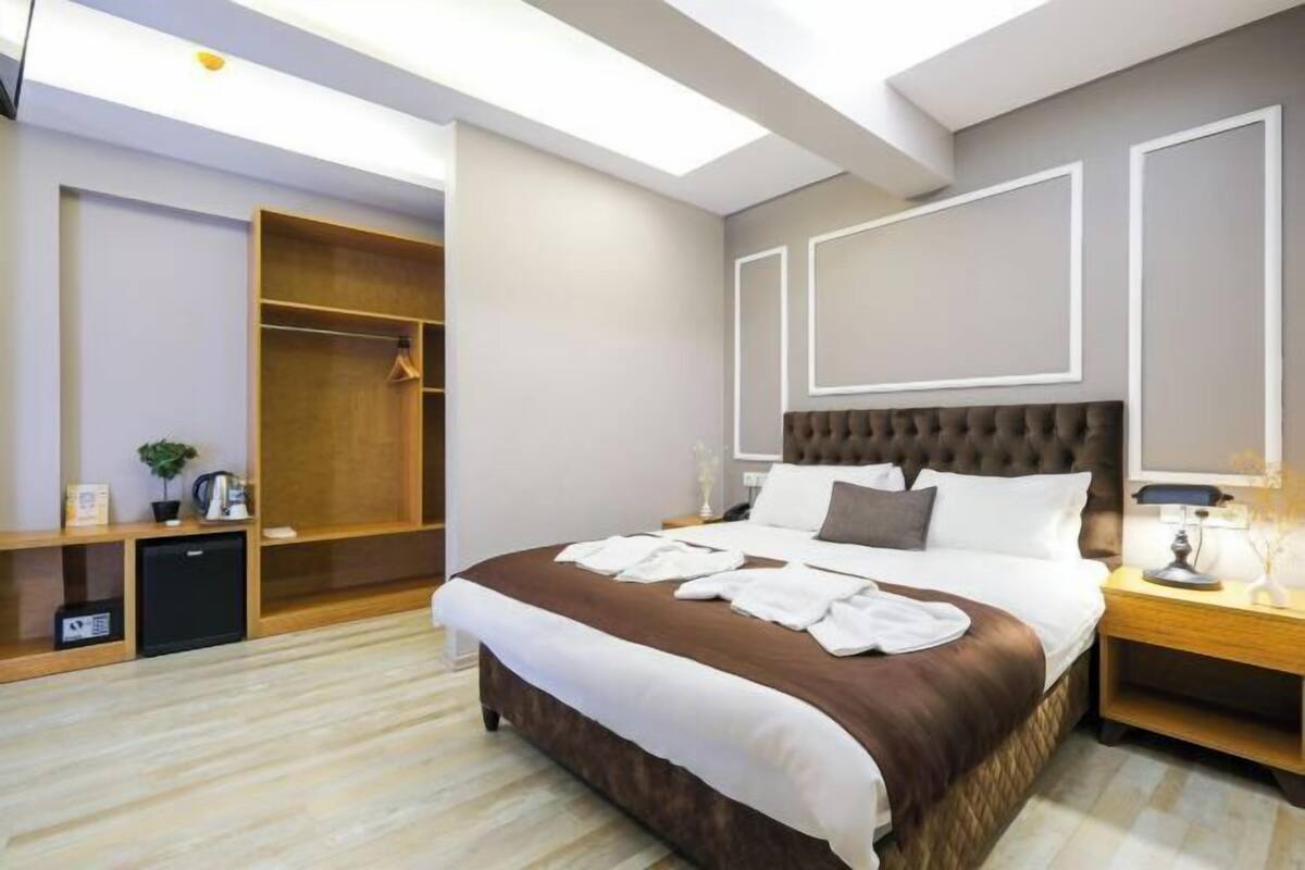 A hotel room with a large bed, a wardrobe, a bedside table, and a desk with a lamp.