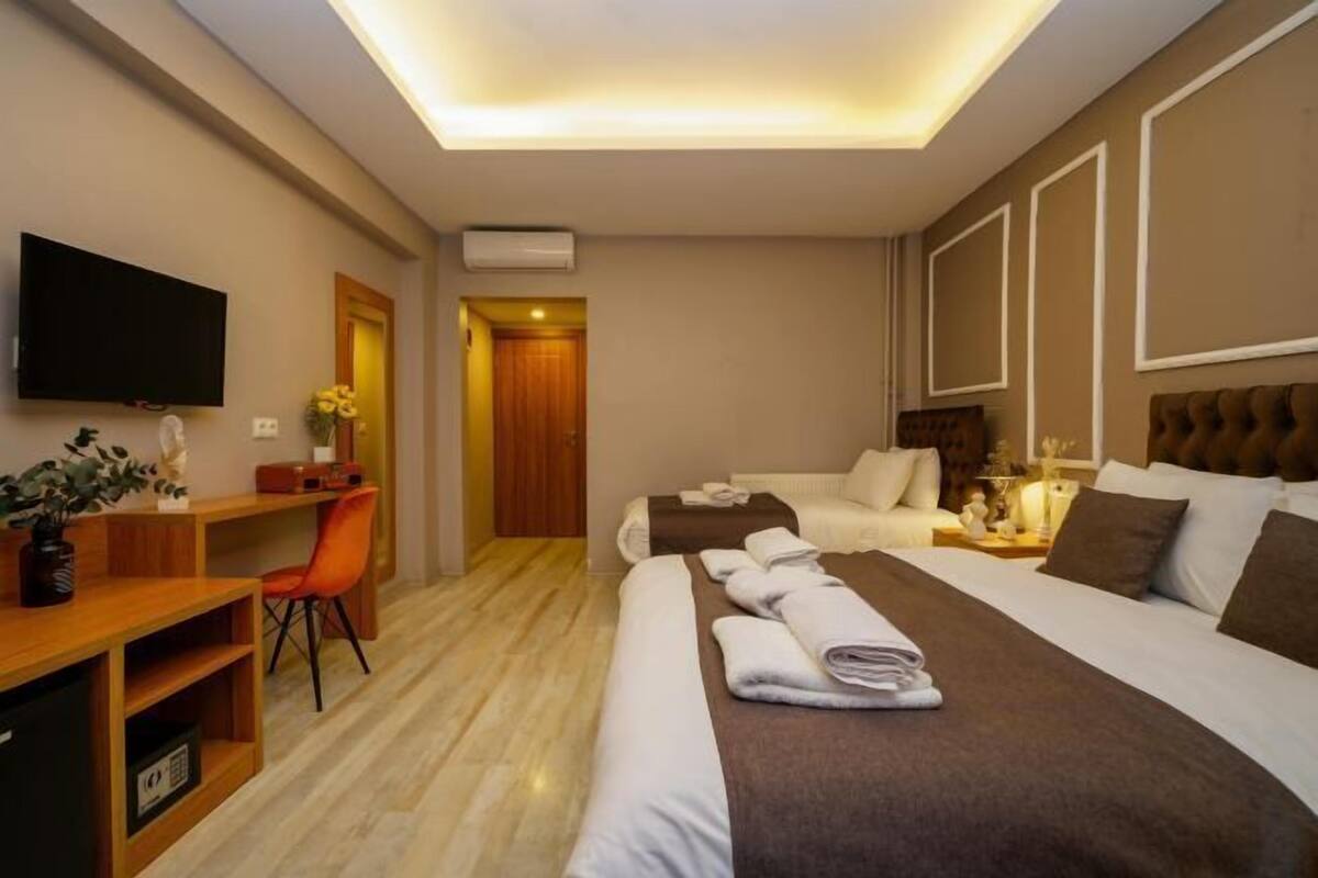A hotel room with a flat-screen TV, a desk with a chair, two beds, and a bedside table with a lamp.
