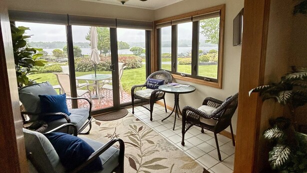 A room with a ceiling fan, large windows, a patio area with outdoor furniture, and a view of a lake.