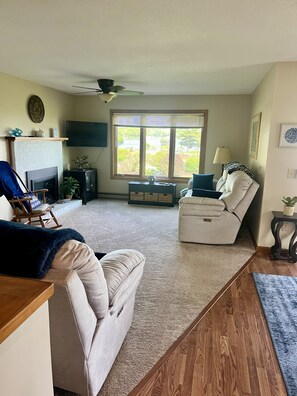 A living room with a fireplace, a sofa, a recliner, a TV, and a large window.