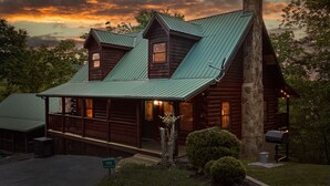 A log cabin with a steeply pitched roof, a chimney, and a porch with railings. - Mountain Escape Book Now (Pigeon Forge)