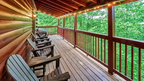 A wooden deck with benches and string lights, overlooking a forested area. - Mountain Escape Book Now (Pigeon Forge)