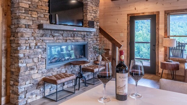 A stone fireplace with a TV, seating, and wine glasses. - Raccoon Ridge Retreat - Gatlinburg Mountain Escape (Gatlinburg)