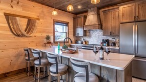 A wooden cabin-style kitchen with a central island, bar stools, and a stainless steel refrigerator. - Raccoon Ridge Retreat - Gatlinburg Mountain Escape (Gatlinburg)