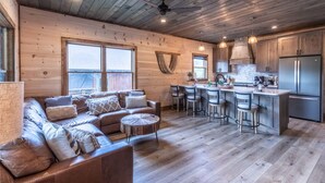 A spacious living area with a wooden ceiling, a sofa set, a coffee table, and a kitchen area with bar stools and a refrigerator. - Raccoon Ridge Retreat - Gatlinburg Mountain Escape (Gatlinburg)
