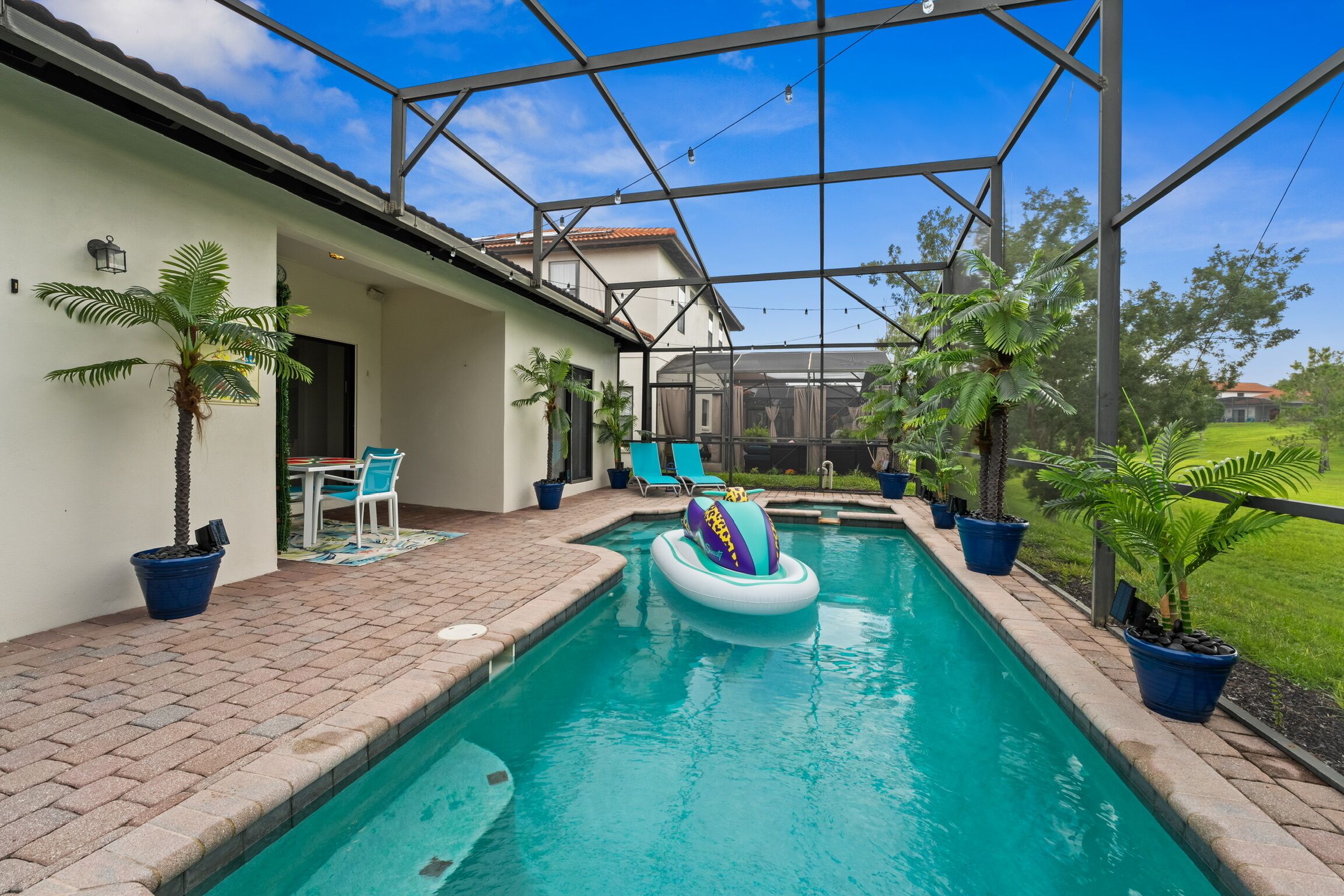 A swimming pool with a glass enclosure, surrounded by potted plants and outdoor furniture.