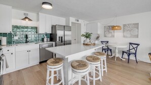 A modern kitchen with white cabinetry, a large island with stools, stainless steel appliances, and a green backsplash.