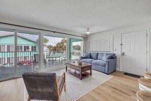 A spacious living room with a large sliding glass door, a blue sofa, a wooden coffee table, and a wicker chair.