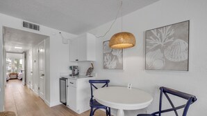 A modern kitchen with white cabinets, a round white table, and two blue chairs.