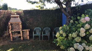 A brick barbecue grill, three green plastic chairs, and a hedge with hydrangea flowers. - Marjolaine Bed and Breakfast on the ground floor (Lourdes)