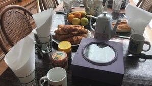 Une table à manger où sont disposés divers aliments pour le petit-déjeuner, notamment des croissants, des fruits et une théière.
