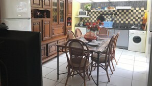 A kitchen with a dining table, chairs, a refrigerator, a washing machine, and a microwave. - Marjolaine Bed and Breakfast on the ground floor (Lourdes)