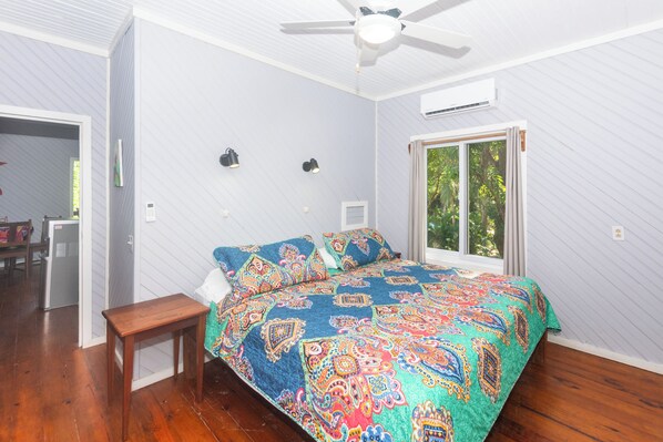 A bedroom with a bed, a wooden bench, a ceiling fan, and a window with curtains.
