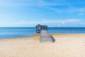 A wooden pier leading to a small structure with a thatched roof, overlooking a calm sea.