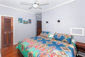 A bedroom with a bed, wooden door, ceiling fan, and two wall-mounted light fixtures.
