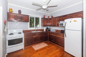 A kitchen with wooden cabinets, a white refrigerator, a stove, and a ceiling fan.