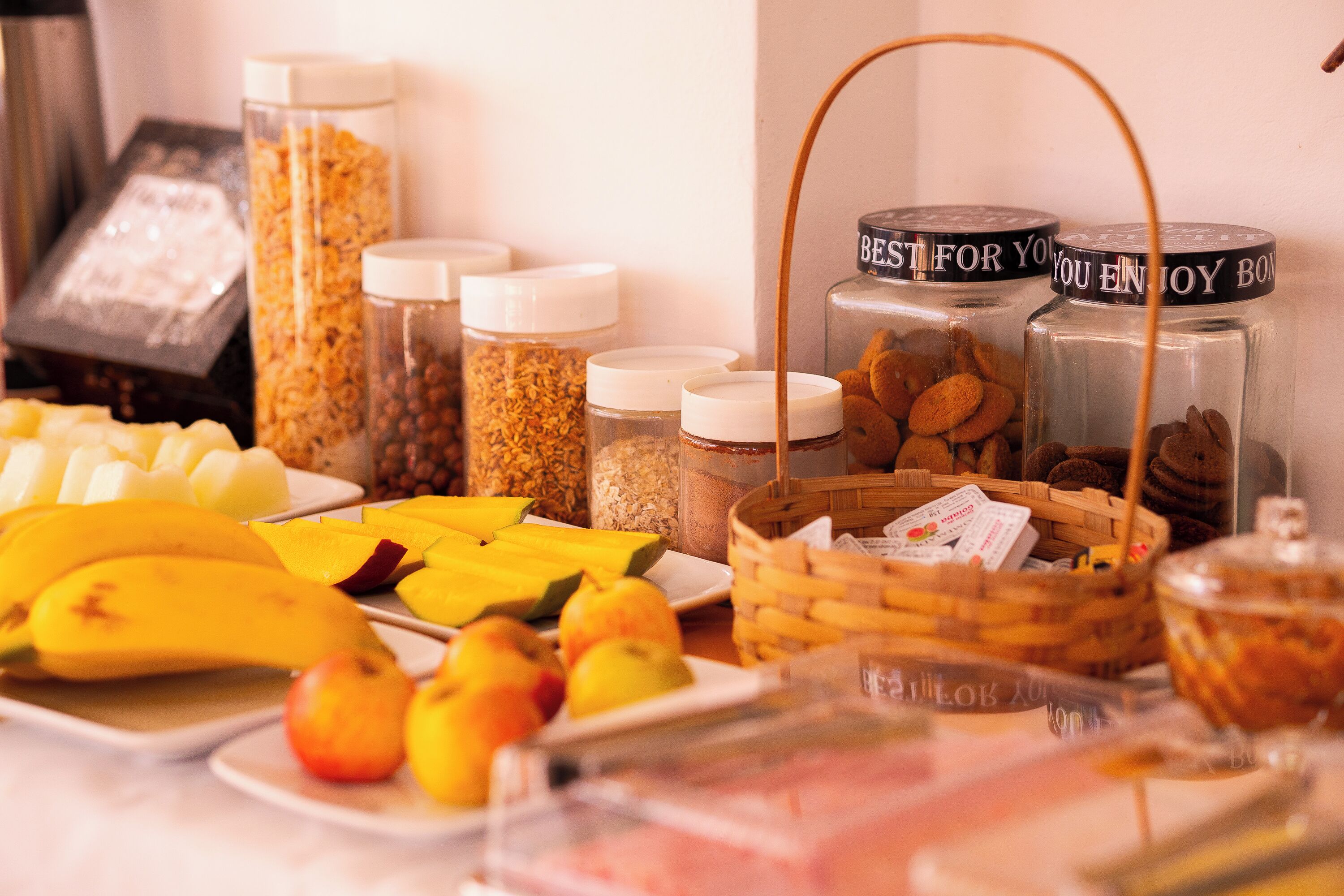 Um buffet de café da manhã com diversas frutas, cereais e produtos de panificação.