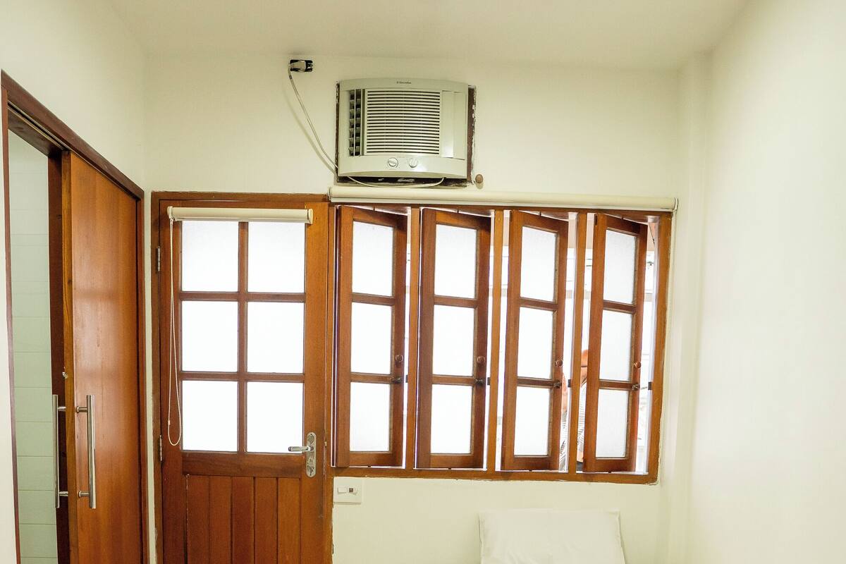 A small, clean room with two beds, a refrigerator, and an air conditioning unit.