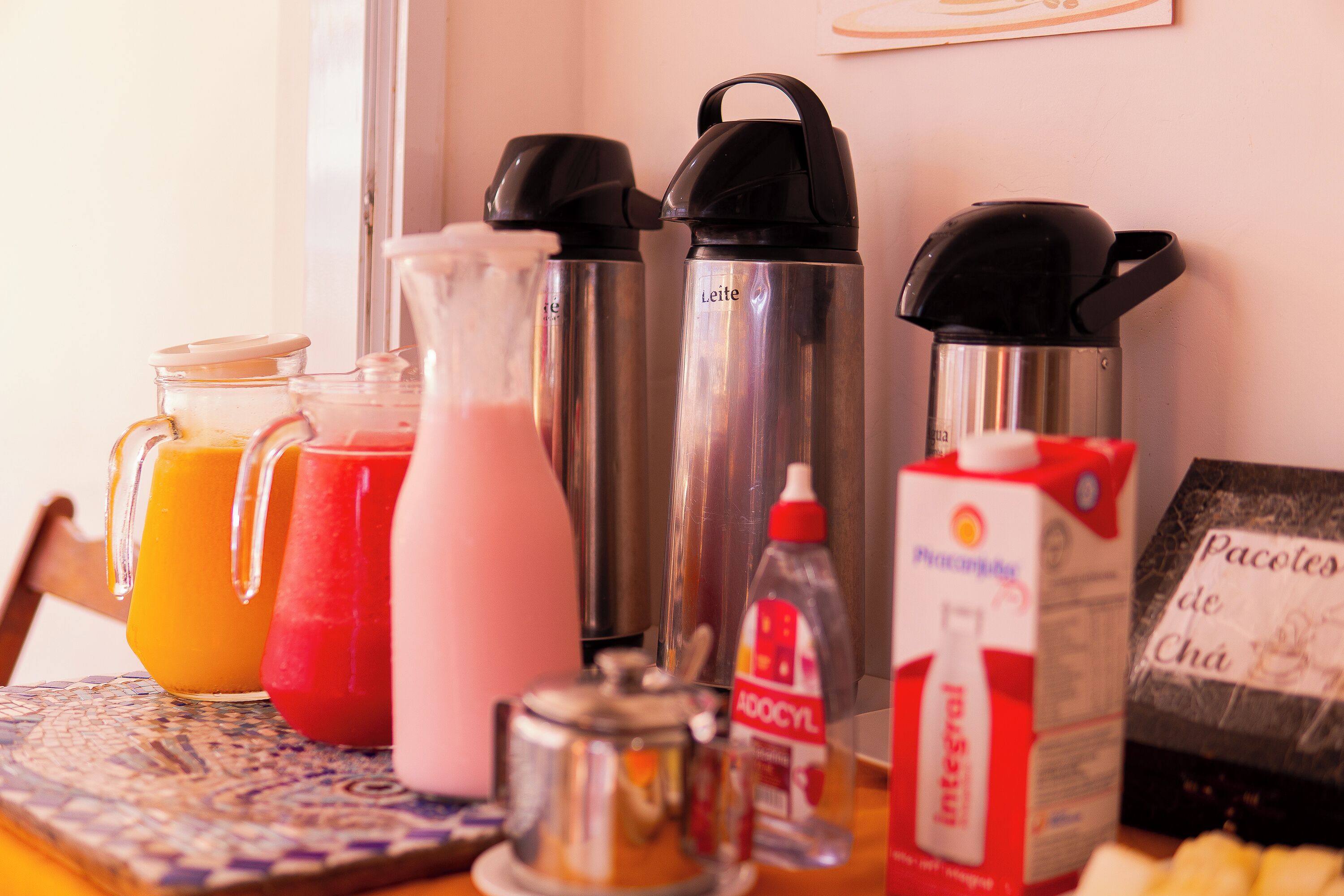 A breakfast table with two insulated water bottles, a pitcher of orange juice, a carton of milk, a bottle of dish soap, and a box of pastries.