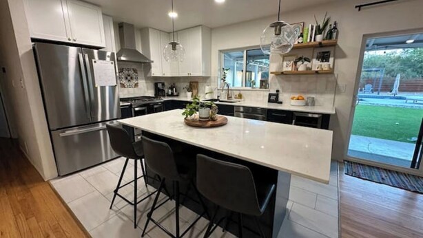 A modern kitchen with stainless steel appliances, a central island with bar stools, pendant lighting, and a view of the outdoors. - Updated! - The Stratford Resort: Pool & Spa (Tucson)