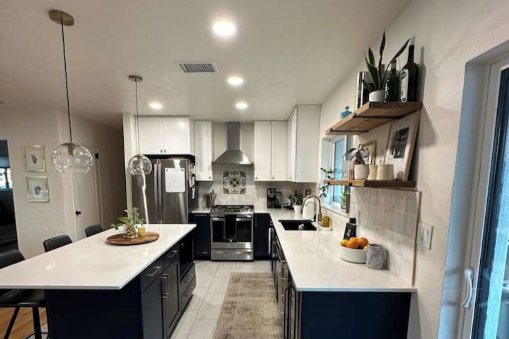 Une cuisine moderne avec des plans de travail blancs, des meubles de rangement sombres, des appareils électroménagers en acier inoxydable et des luminaires suspendus.
