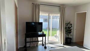 A hotel room with a bed, a TV on a stand, a potted plant, and a view of the outdoors through a sliding glass door. - Updated! - The Stratford Resort: Pool & Spa (Tucson)