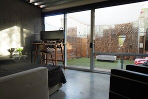 Una habitación moderna con cama, escritorio con televisor y un amplio ventanal corredero que da a un jardín.