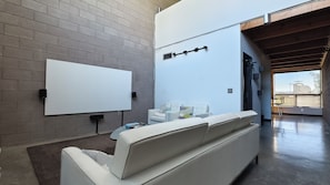 Uma sala de estar moderna com um sofá branco, uma mesa de centro de vidro e um quadro branco na parede.