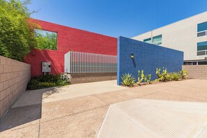 A modern building with a red and blue tiled facade, a gated entrance, and a paved courtyard with cacti.