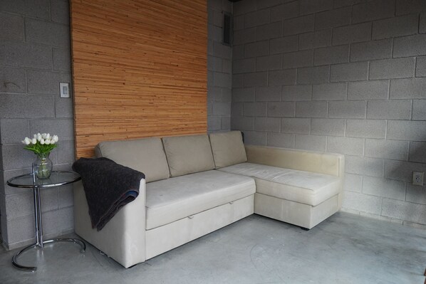 Una sala de estar moderna con un sofá seccional color beige, una pequeña mesa redonda con un jarrón de flores y un panel de madera en la pared.