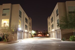 A nighttime view of a modern building with multiple garage doors, a well-lit entrance, and a clear sky. - Downtown Modern Loft Steps from Roosevelt Row-Smart Living, Garage, Pool & Yard (Phoenix)