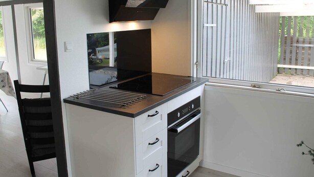 A compact kitchen with a black countertop, white cabinetry, and a window with a view of a wooden fence. - 4 Star Holiday Home in Dannemare (Dannemare)